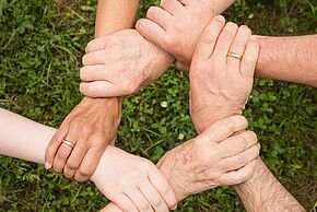 6 mains différents tenant le poignet de la personne de droite. Le tout forme un cercle.